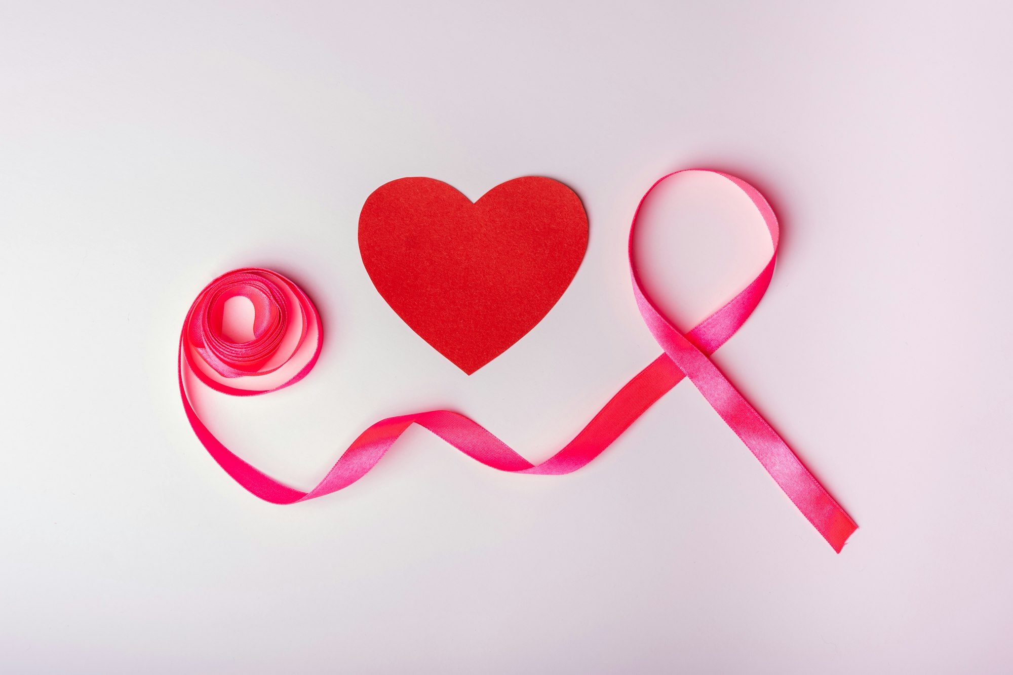 Pink ribbon as a symbol of breast cancer and a heart on a pink background. Women's health concept.